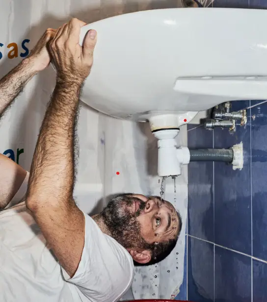 Plumber repairing a leaking bathroom sink drain with water dripping under the basin in Mislata, Valencia.